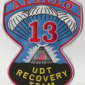 May include: Embroidered patch featuring the Apollo 13 mission. The design includes the number 13 in red, parachutes, and a depiction of a spacecraft with the American flag. The text "APOLLO" and "UDT RECOVERY TEAM" are also present.