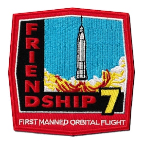 Op de afbeelding: Geborduurde patch met een rode rand en een blauwe achtergrond. De patch toont een lancerende raket, met de tekst "FRIENDSHIP 7" in rood en geel. De tekst "FIRST MANNED ORBITAL FLIGHT" is ook opgenomen.