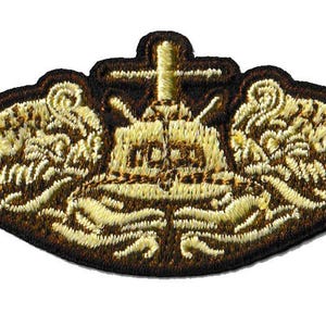 Könnte beinhalten: Gestickter Aufnäher mit einem detaillierten Design in Gold- und Brauntönen. Der Aufnäher hat ein zentrales Emblem mit einem Kreuz, flankiert von stilisierten wellenartigen Mustern. Die Ränder sind in dunklerem Braun umrandet.