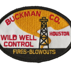 May include: A white oval patch with a black border. The patch has red text that reads "BUCKMAN CO. HOUSTON" and "WILD WELL CONTROL" and gold text that reads "FIRES - BLOWOUTS". A black and white illustration of an oil rig with smoke is in the centre of the patch.