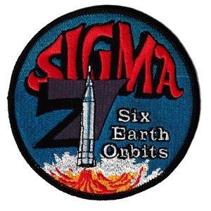 May include: Embroidered patch featuring a rocket launching from a fiery base, with the text "SIGMA 7" in red and "Six Earth Orbits" in white. The patch has a blue background and a black border.
