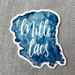 May include: A blue watercolor sticker with the text "Mille Lacs" in white cursive lettering.