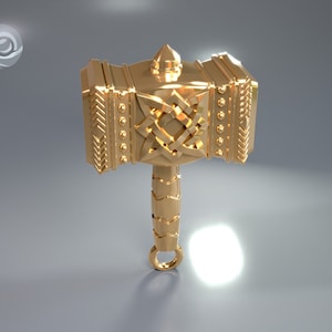 Puede incluir: Un colgante de martillo de metal dorado con intrincados diseños de nudos y una parte superior puntiaguda. El martillo tiene un bucle en la parte inferior para sujetarlo a una cadena o cordón.