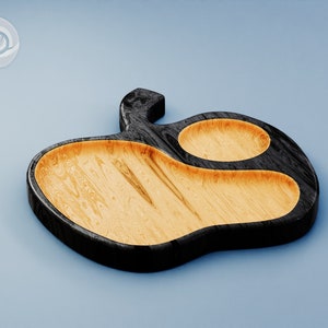 May include: A wooden serving tray shaped like an apple with two separate compartments. The tray is black with a natural wood finish.