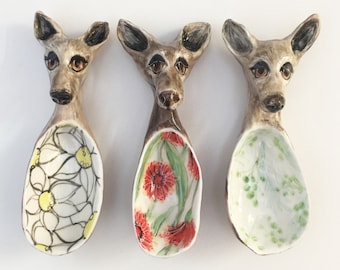 Puede incluir: Tres cucharas de cerámica con forma de cabeza de animal con diseños florales. Las cucharas son marrones y blancas con patrones florales en tonos amarillos, rojos y verdes.
