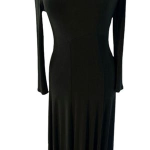 Pode incluir: Um vestido preto liso de manga comprida com gola alta, corpete justo e saia rodada que chega ao comprimento midi. A peça é construída com detalhes de costura vertical ao longo do tronco frontal e dos painéis da saia.