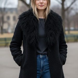 May include: A black textured coat featuring a large, fluffy faux fur collar, long sleeves, and two side pockets. The coat is worn over a dark gray t-shirt and blue denim jeans. The garment has a single button closure at the front and a mid-thigh length.