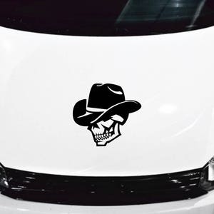 May include: A black and white skull wearing a cowboy hat. The skull is wearing a wide-brimmed hat with a band around it. The skull is facing to the left. The image is on a white background.
