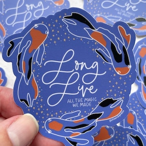 May include: A blue sticker with two orange and black fish swimming around the text "Long Live" with the words "All the magic we made" underneath. The sticker has a gold glitter background.