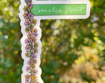 May include: A sticker with a green sign that says "Cornelia Street" with a vine of pink and orange flowers on a white background.