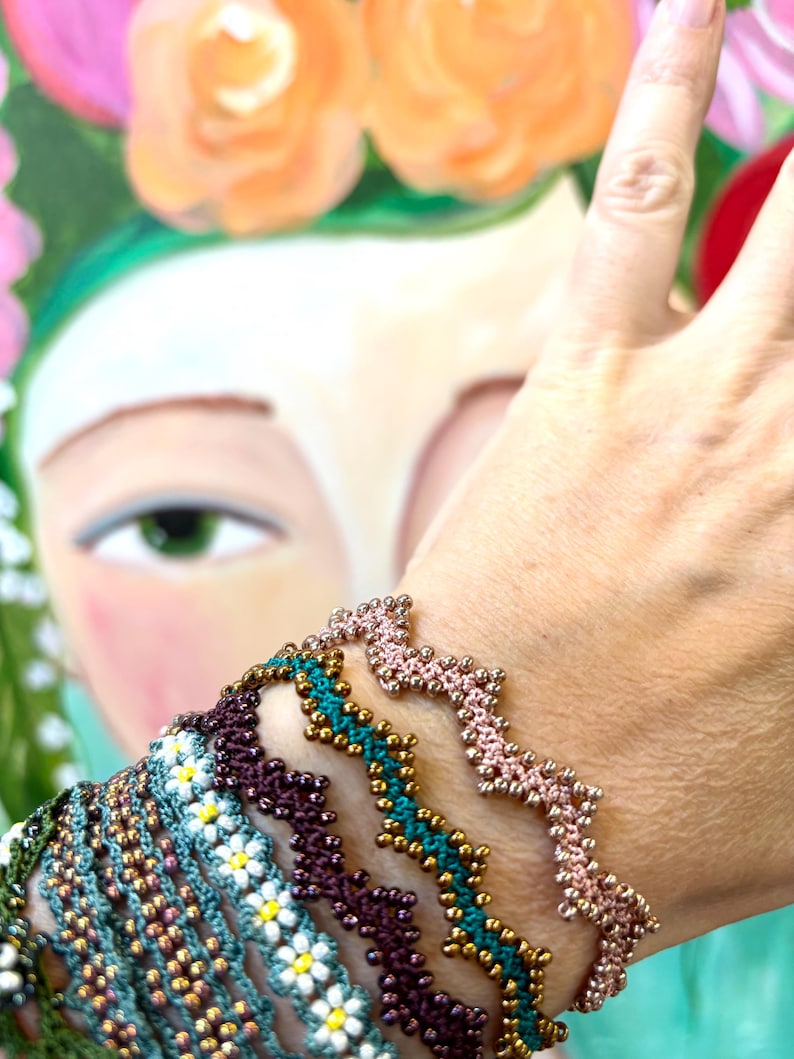 May include: A collection of beaded bracelets in various colors, including teal, purple, and pink. The bracelets feature intricate patterns and gold-colored beads. The background is a painting of a woman with flowers in her hair.
