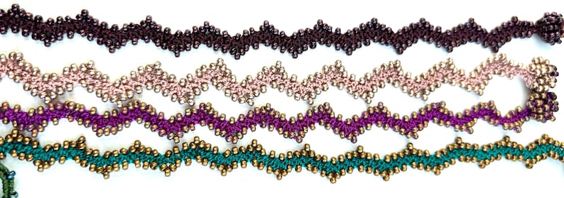 May include: Five beaded zig-zag trim samples in various colors. The colors include dark brown, light pink, purple, and teal. Each trim is adorned with small, gold-colored beads. The trim is likely used for embellishing clothing or craft projects.