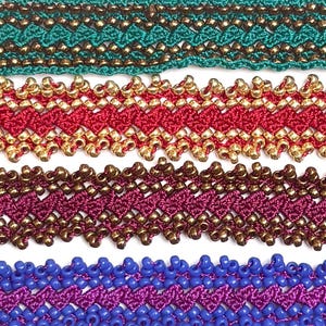 Op de afbeelding: Vier horizontale stroken geweven textielband met ingewikkelde zigzagpatronen. De banden zijn uitgevoerd in de kleuren groenblauw, rood, donker magenta en paars, elk versierd met rijen ingeweven metallic gouden of bronzen kraaltjes.