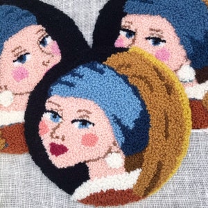 Op de afbeelding: Drie ronde wandkleden met naaldvilt, met een portret van een vrouw met een blauwe hoofddoek en een parel oorring. De portretten zijn in moderne stijl met felle kleuren en eenvoudige lijnen.