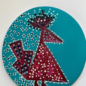 May include: A teal, circular, decorative ornament featuring a stylized bird design. The bird is primarily burgundy with white and pink dot accents. The background has white and black dot patterns.