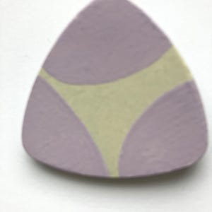 Puede incluir: Un plato triangular de cerámica, con base lavanda y un diseño curvo verde claro en el centro. El plato está sobre un fondo blanco. El diseño recuerda a una prenda interior.
