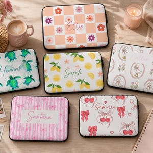 Könnte beinhalten: Sechs rechteckige Laptoptaschen mit abgerundeten Ecken, jede mit einem einzigartigen Muster und einem personalisierten Namen. Die Designs umfassen ein pfirsichfarbenes Karomuster mit Blumen, grüne Meeresschildkröten, Zitronen, Enten und Kirschen.