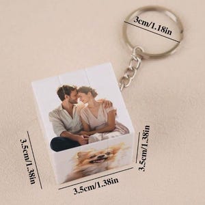 May include: White photo cube keyring with a couple and a dog on it. The cube measures 3.5 cm on each side. The keyring is attached to a silver metal ring.