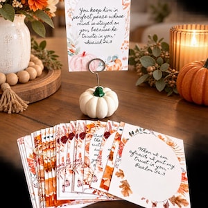 May include: A white pumpkin-shaped card holder with a metal wire clip holding a rectangular card featuring orange and brown floral illustrations and the text: You keep him in perfect peace whose mind is stayed on you, because he trusts in you. Isaiah 26:3.