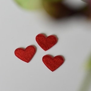 Könnte beinhalten: Drei rote Filzherzen auf weißem Hintergrund. Die Herzen sind in Dreiecksform angeordnet.