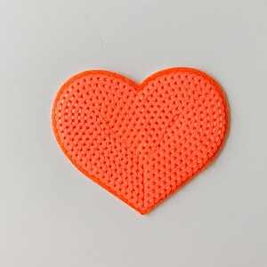 Könnte beinhalten: Ein leuchtend orangefarbener herzförmiger Patch aus Pailletten.