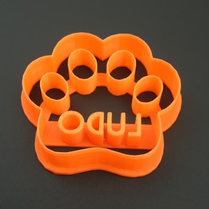 May include: Orange plastic cookie cutter shaped like a paw print with the word "LUDO" written inside.
