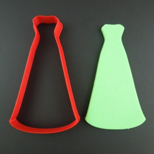 Può includere: Tagliapasta in plastica rossa a forma di vestito, accanto a un ritaglio di pasta di zucchero verde a forma di vestito.