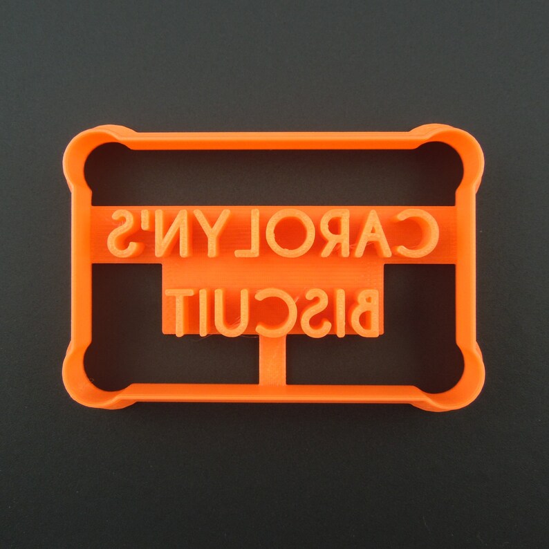 May include: Orange plastic cookie cutter shaped like a rectangle with the words "CAROLYN'S BISCUIT" embossed on it.