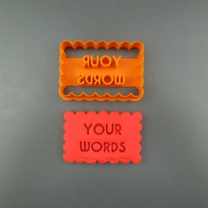 Peut inclure: Emporte-pièce en plastique orange avec les mots "YOUR WORDS" en sens inverse. Un biscuit rouge est présenté avec les mêmes mots dans la bonne orientation.
