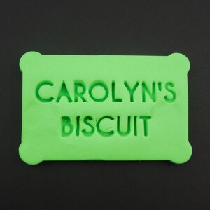 May include: A bright green rectangular cookie cutter with the text "CAROLYN'S BISCUIT" embossed on the front.