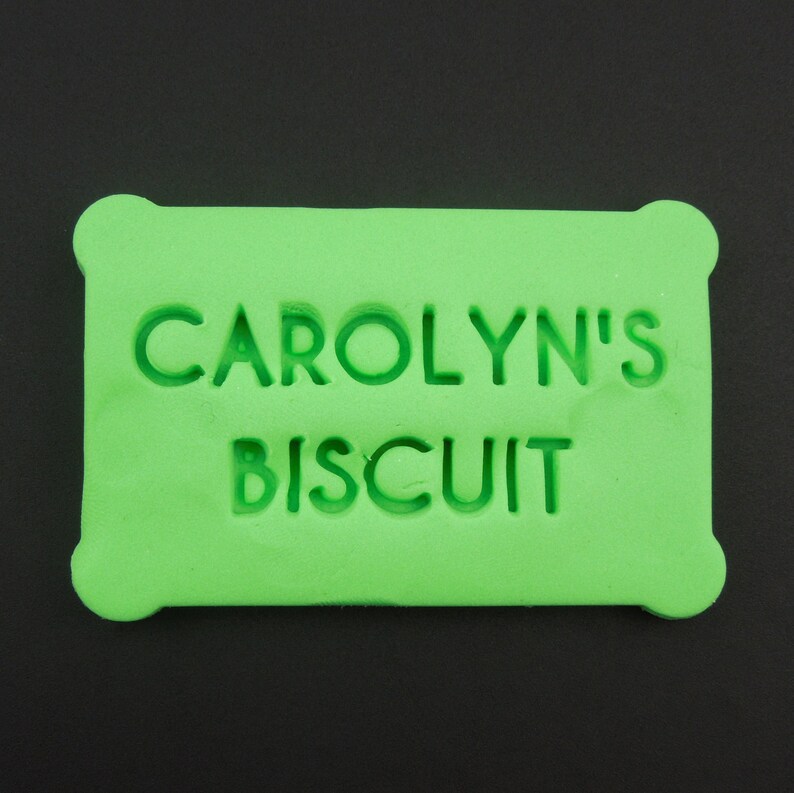 May include: A bright green rectangular cookie cutter with the text "CAROLYN'S BISCUIT" embossed on the front.