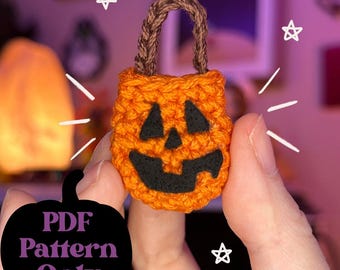May include: An orange crocheted pumpkin-shaped bag with a black face and a brown handle. The bag is held in a person's hand. The text "PDF Pattern Only" is in a black pumpkin shape.