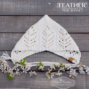 May include: Cream-coloured knitted pixie bonnet with a leaf pattern. The bonnet has a pointed top and a braided tie with tassels. The text "FEATHER PIXIE BONNET" is displayed at the top. The bottom of the image shows the text "White Feather Handmade" and a website address.