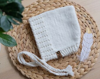 May include: White crocheted baby bonnet with a tie, featuring a small brown leather tag with the text "Wee WF".