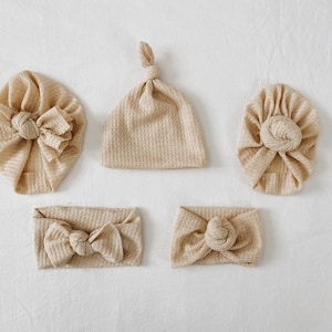 Op de afbeelding: Set van vier beige wafel gebreide hoofdbanden en hoeden met geknoopte details. De hoofdbanden zijn ontworpen om te worden gedragen als een hoofdband of een tulband. De hoeden zijn ontworpen om te worden gedragen als een beanie of een slouchy hoed.