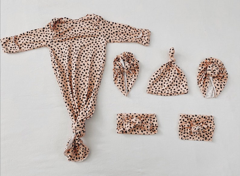 K&ouml;nnte beinhalten: Ein Set Babykleidung in einem beige-schwarzen Gepardenmuster. Das Set beinhaltet ein gebundenes Kleid, ein gebundenes Stirnband, eine gebundene M&uuml;tze und zwei Stirnb&auml;nder.