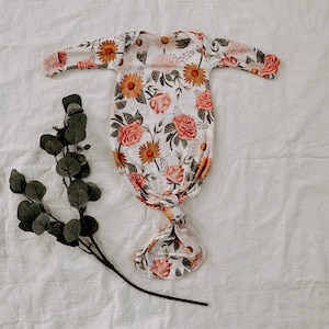 May include: A white knotted gown with a floral print featuring pink roses, yellow sunflowers, and green leaves.