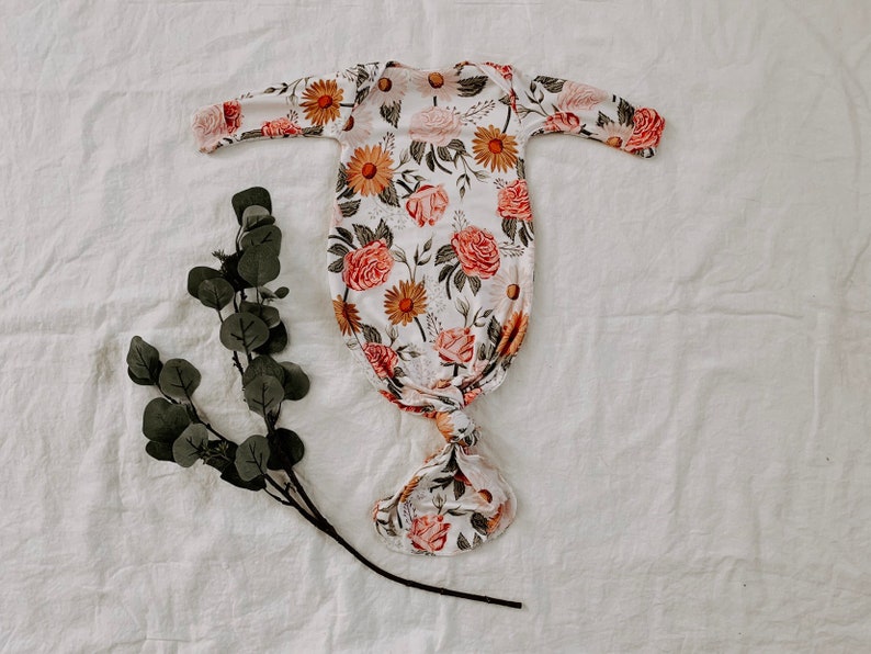 May include: A white knotted gown with a floral print featuring pink roses, yellow sunflowers, and green leaves.