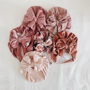 Op de afbeelding: Zes verschillende stoffen hoofdbanden met strikken in verschillende tinten roze en bruin. De hoofdbanden zijn gemaakt van een zachte, rekbare stof en hebben een comfortabele pasvorm.