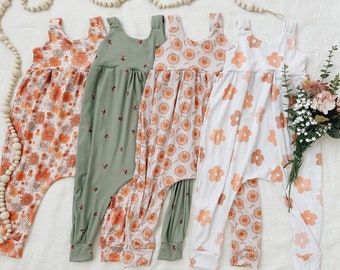 May include: Four sleeveless baby jumpsuits with floral patterns. The jumpsuits are in shades of white, green, and orange. The floral patterns include daisies and other small flowers.