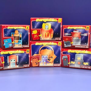 May include: A collection of six "Changeables" toy boxes, each featuring a different robot-like character. The boxes are red with yellow text and include the McDonald's logo. The characters have names like "Torrus" and "Boo Bot".