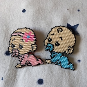 Pode incluir: Duas figuras de bebês feitas de contas, uma com um vestido rosa e uma flor na cabeça, a outra com um traje azul. As figuras são feitas de pequenas contas e são costuradas juntas.