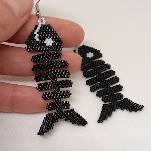 May include: A pair of black and white beaded fish bone earrings. The earrings are made with small black beads and white beads for the eyes.