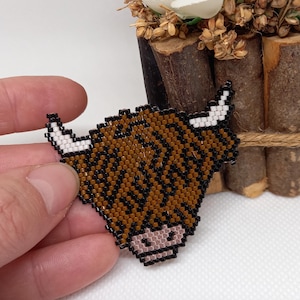 May include: A brown and black beaded Highland Cow head with white horns. The cow is beaded in a pixelated style.