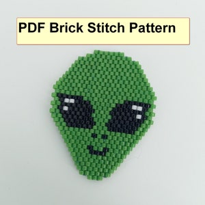 May include: A green alien face bead pattern in brick stitch. The pattern includes black and white beads for the eyes and a black bead for the mouth.