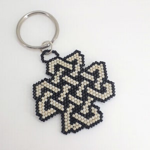 May include: A black and white beaded keychain shaped like a four-leaf clover. The keychain has a silver key ring.