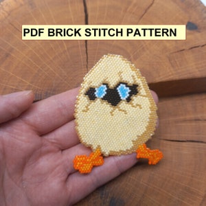 May include: A beaded chick with blue eyes and orange feet. The chick is wearing sunglasses. The beadwork is in a brick stitch pattern. The chick is sitting on a wooden surface. The text "PDF BRICK STITCH PATTERN" is at the top of the image.