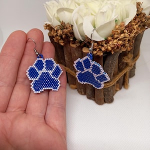 May include: A pair of blue and white beaded paw print earrings. The earrings are hanging from silver hooks.