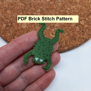 May include: A green beaded frog created using the brick stitch technique. The frog has white eyes and is displayed against a corkboard background. The text "PDF Brick Stitch Pattern" is in a yellow rectangle.