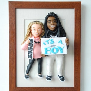 May include: A framed 3D clay sculpture of a couple holding a sign that says "It's a Boy!" The woman is holding an ultrasound image in her left hand. The sculpture is set against a white background.